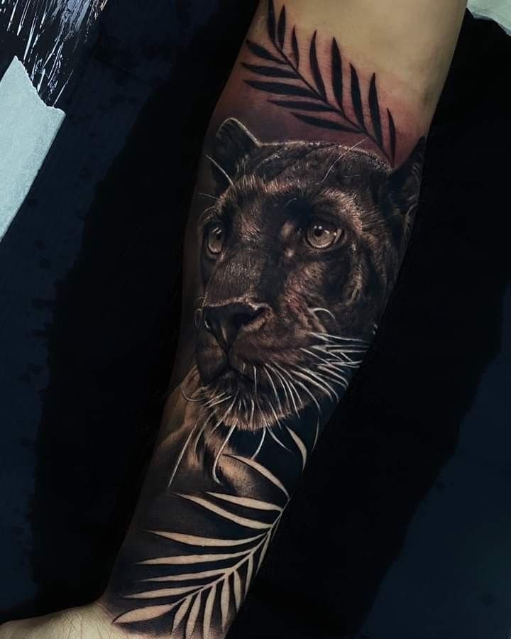 Hình xăm báo đen chi tiết trên cánh tay, phong cách blackwork, lá cây, ảnh chất lượng cao.