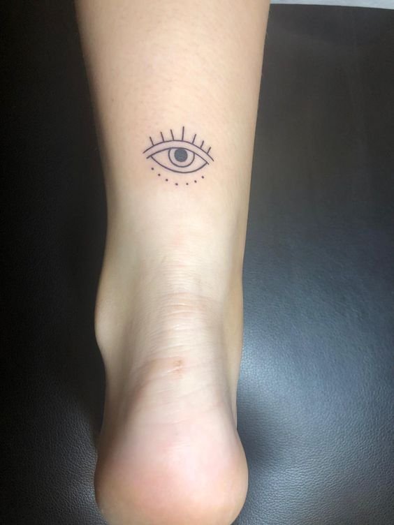 Hình xăm mắt mini ở mắt cá chân, phong cách blackwork, chi tiết đơn giản, ảnh độ phân giải cao.