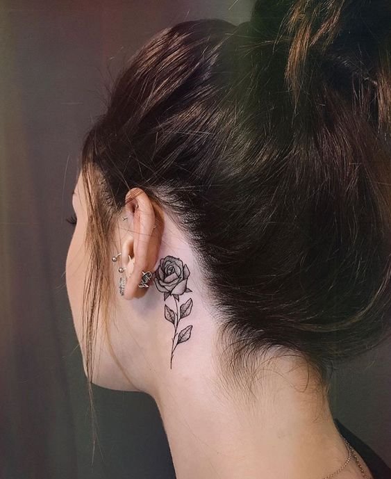 Hình xăm hoa hồng đen mini nổi bật trên làn da trắng Hình xăm hoa hồng mini sau tai, phong cách blackwork, chi tiết rõ nét, độ phân giải HD.